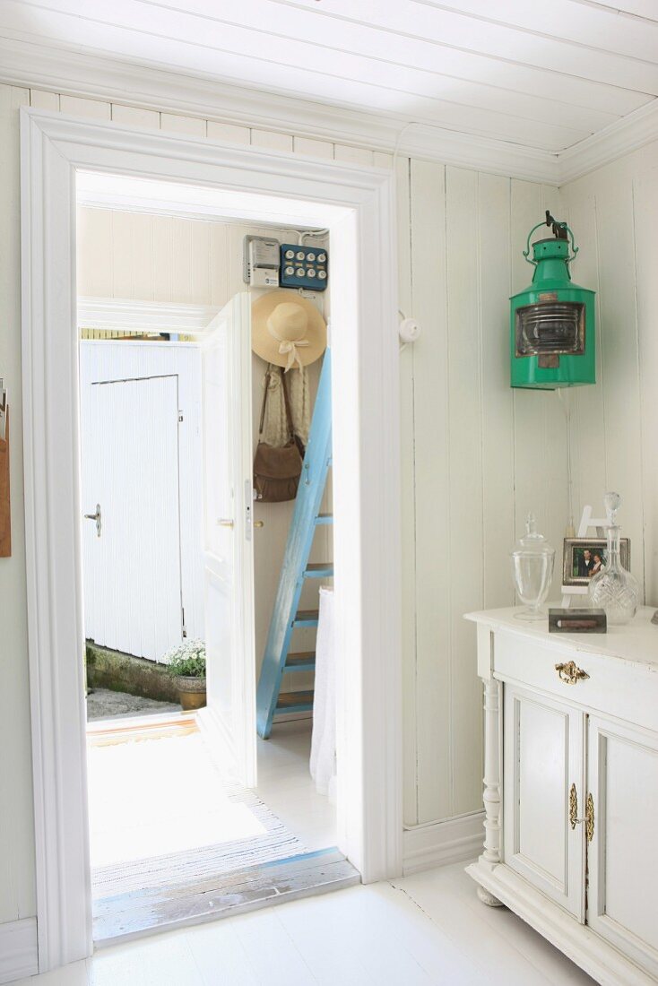 Vorraum eines Sommerhauses mit pastellblauer Holztreppe und kleiner Garderobe mit daran hängendem Sonnenhut und Handtasche