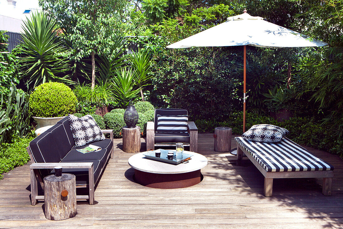 Modern outdoor furniture with black and white upholstery and parasol on wooden terrace in tropical garden