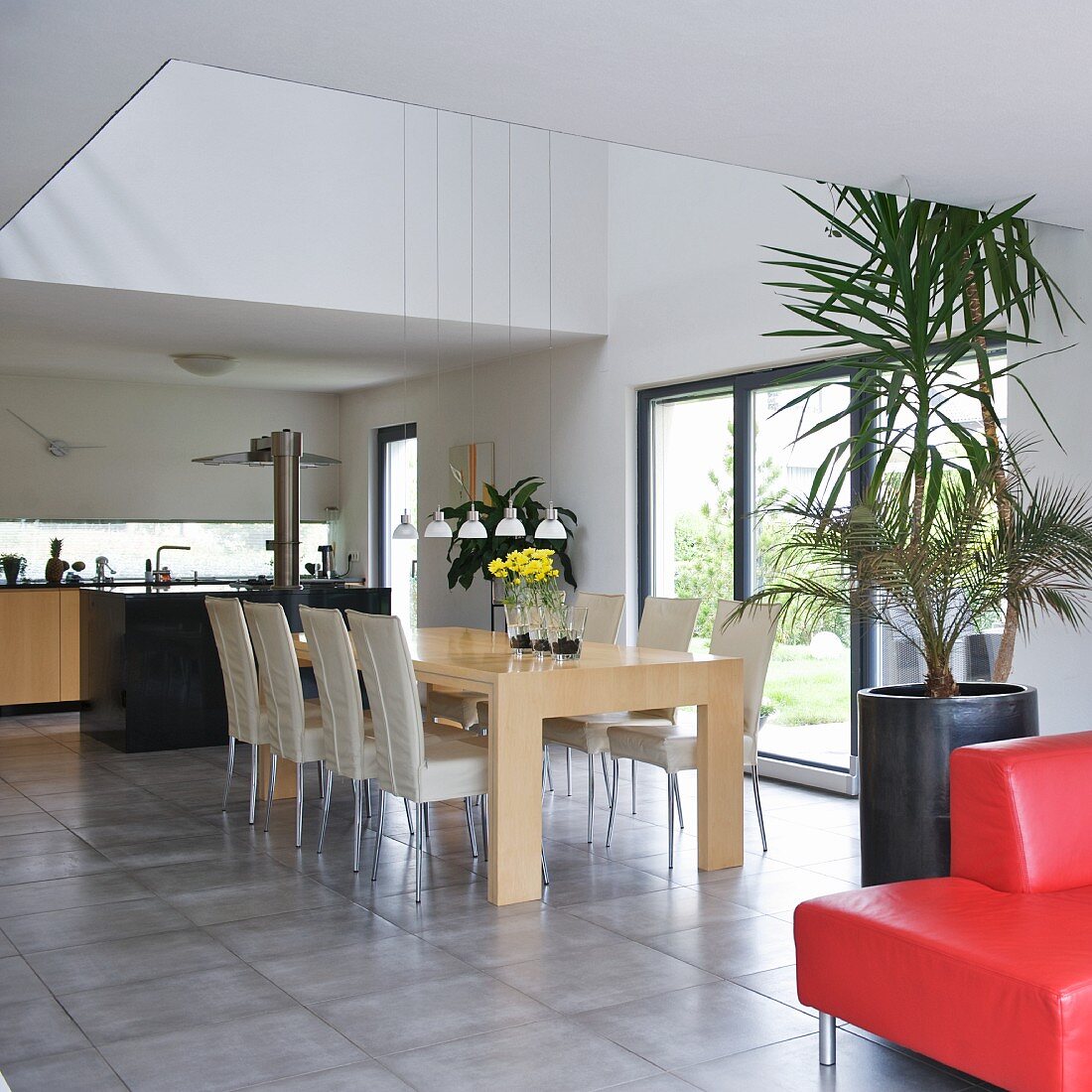Cooler Designer Wohnraum mit Ess- und Kochbereich - Stühle mit hellem Bezug an Holztisch auf hellgrauem Steinboden unter Lichtschacht