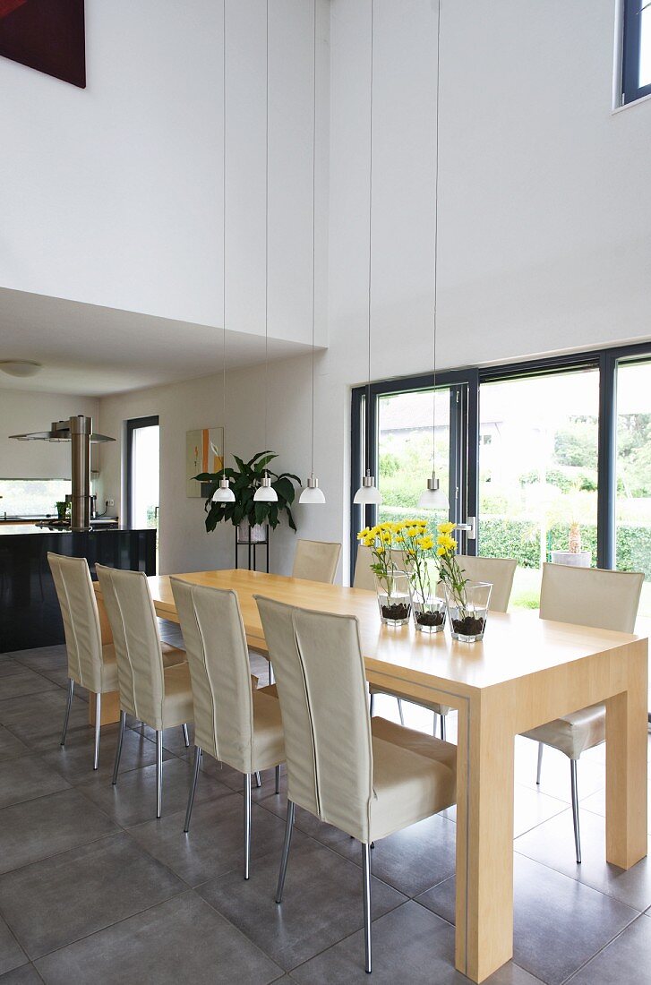 Dining chairs with pale covers and minimalist dining table in pale wood in front of terrace window in contemporary house