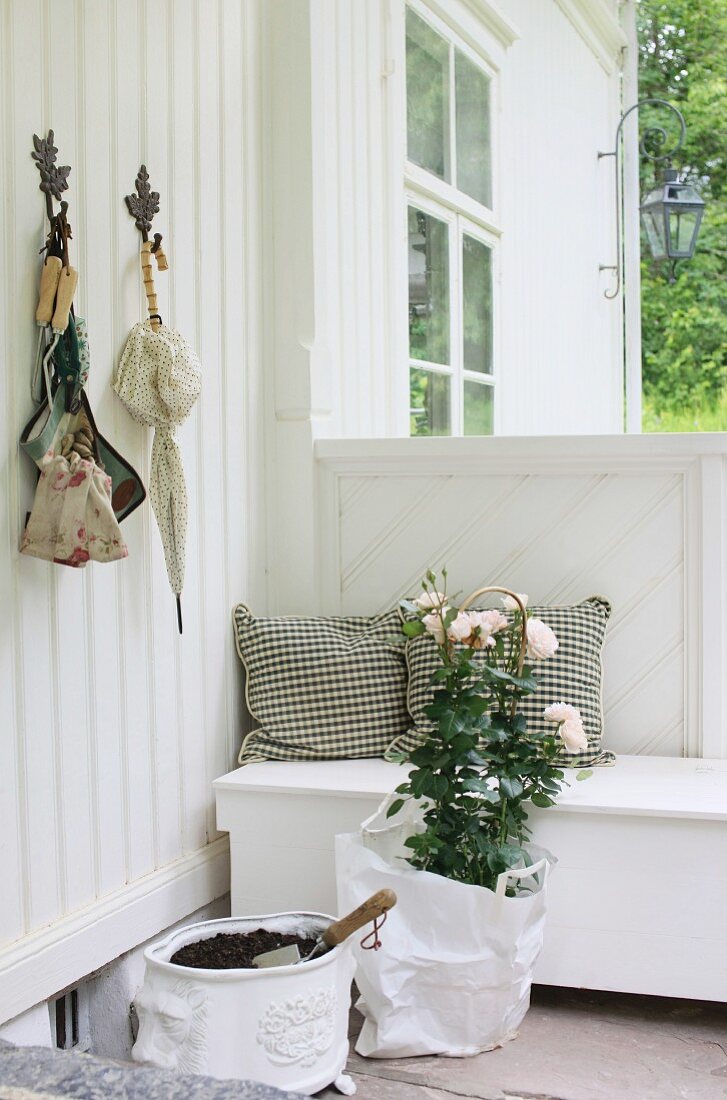 Geschützter Sitzplatz auf der Veranda - Holzsitzbank, Rosenstock und nostalgischer Pflanztopf mit Erde