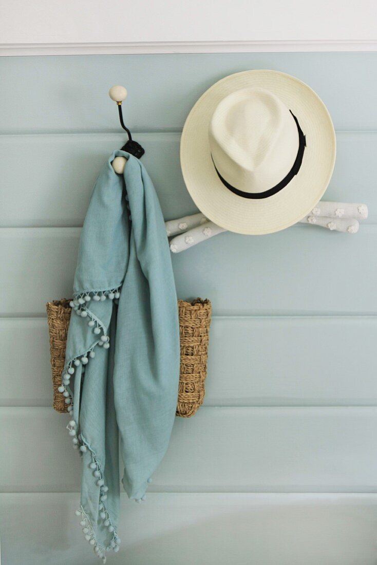 Nostalgische Kleiderhaken an hellblauer Wandverkleidung mit Sommerhut, Schal und Tasche