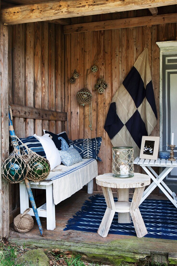 Many scatter cushions on bench against rustic wooden wall, lantern and glass floats in knotted nets