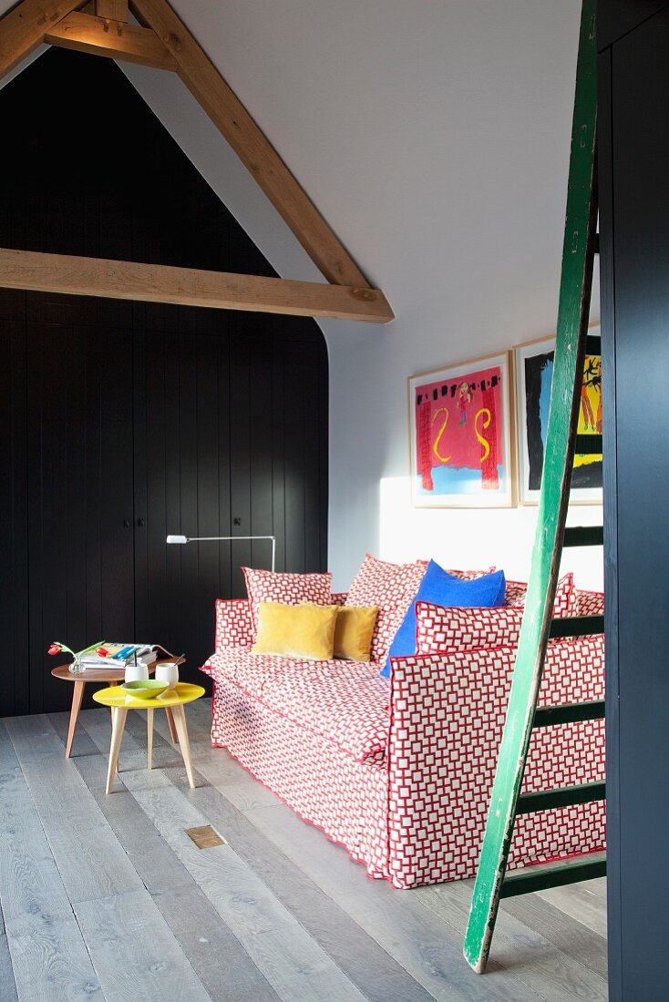 Red and white couch, small retro coffee tables and floor-to-ceiling fitted cupboards with dark grey doors in room with gable ceiling