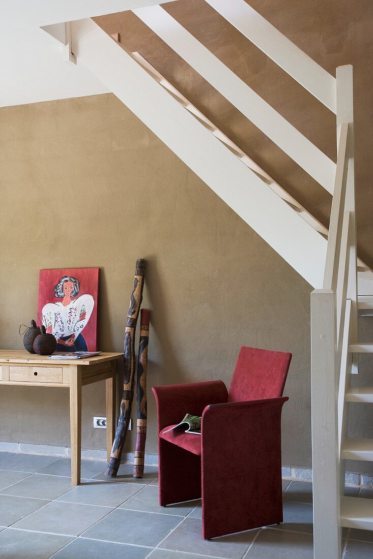 Weiß gestrichene Holztreppe vor grauer Wand und rot bezogener Stuhl neben Wandtisch in modernem Vorraum