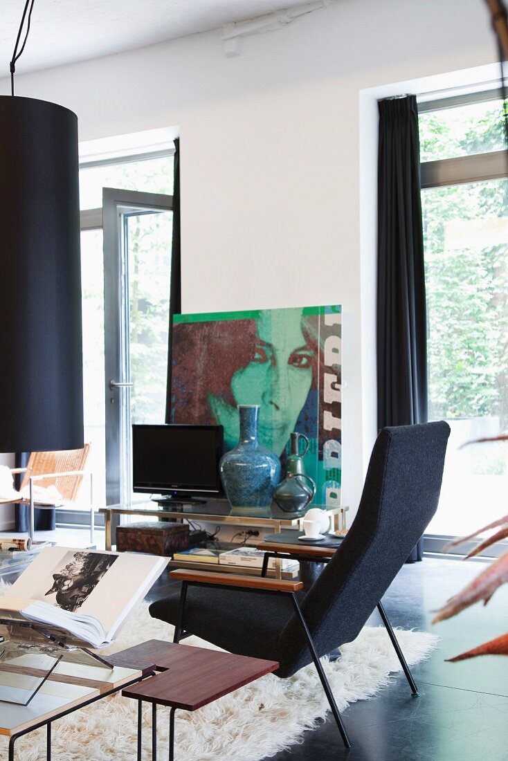 Vintage armchair and side table in bright loft apartment; poster with portrait of woman in background