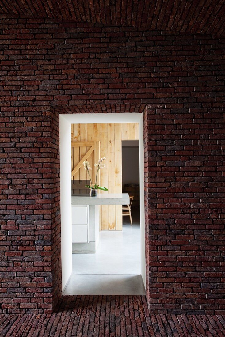 View through opening in brick facade of modern counter in wood-panelled room