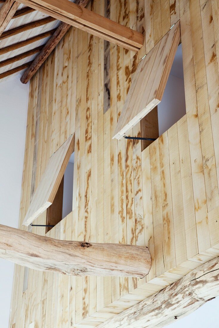 Blick auf Holzwand im Obergeschoss mit geöffneten Fensterluken aus Holz