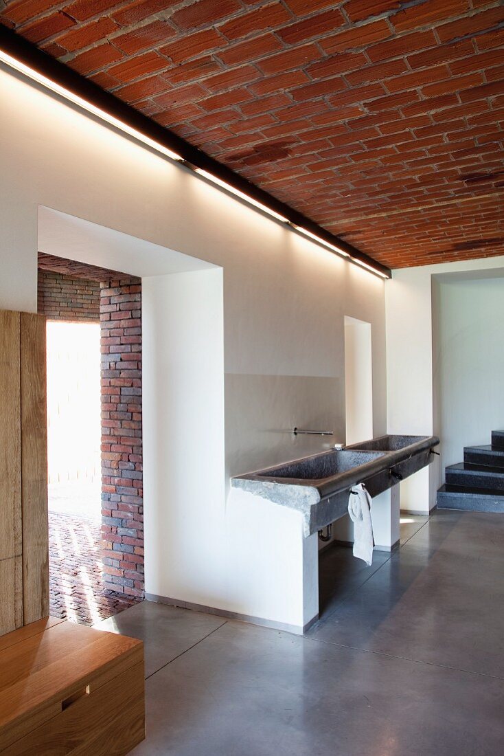 Offener Waschbereich mit trogartigem Waschbecken an Wand im Vorraum mit Durchgängen
