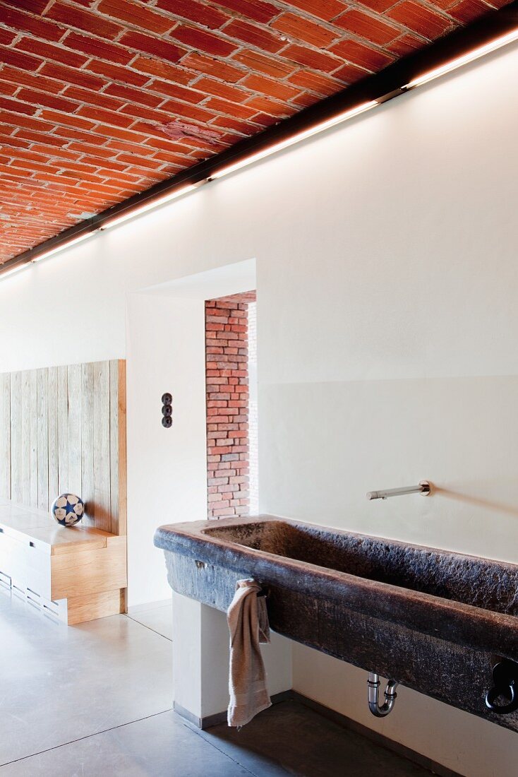 Stone, trough-style washstand against wall in open-plan foyer with brick ceiling