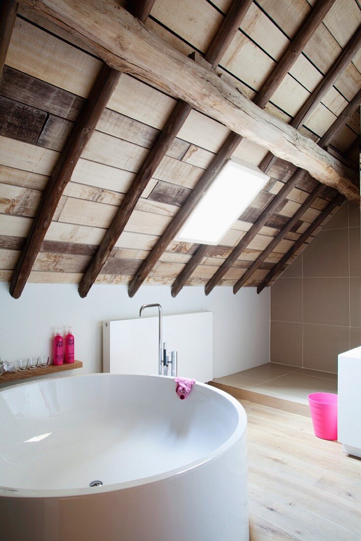 Round bathtub in modern attic bathroom with wooden ceiling
