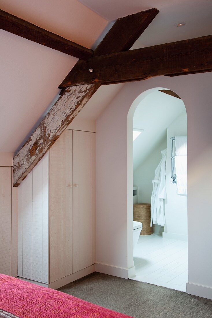 Rustic roof beams in bedroom with fitted wardrobe under sloping ceiling and ensuite bathroom