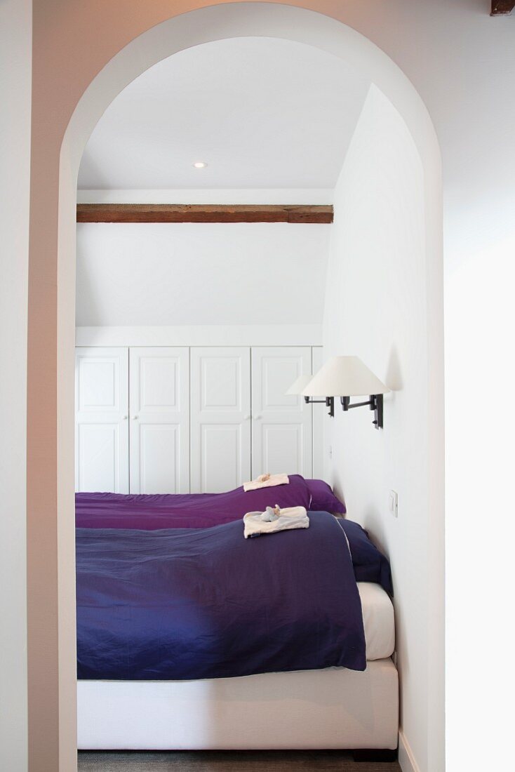 Einzelbetten mit blauer und violetter Bettwäsche in weißem Schlafzimmer mit Einbauschrank unter der Dachschräge