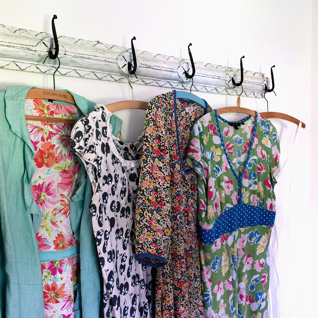 Colourful, floral dresses and pinafores hanging on old, vintage-style coat rack