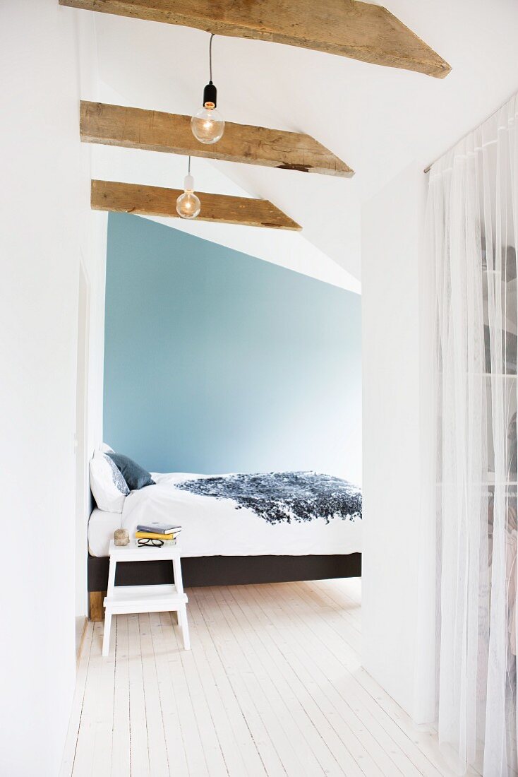 Dachzimmer mit Bett vor blauer Wand und hellem Dielenboden