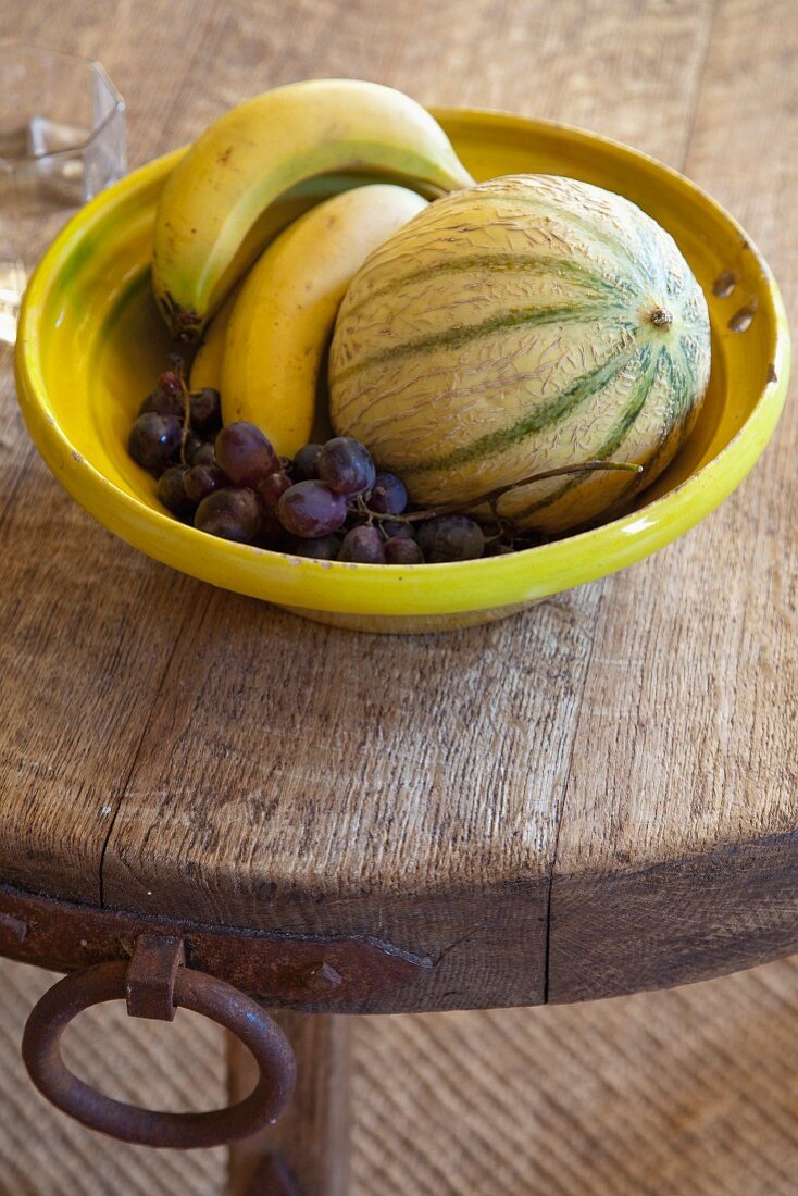 Obst in gelber Schale auf rustikaler Holz Tischplatte mit Metallbeschlag