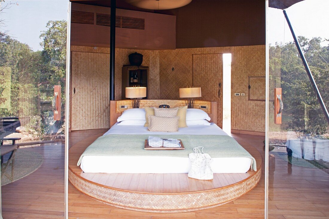 View through open door into elegant bedroom with double bed on curved platform