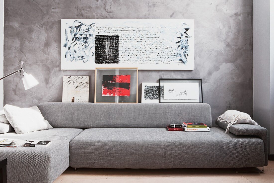 Sitzecke in harmonischen Grautönen mit Sofalandschaft und Schriftbildern vor marmorierter Wand