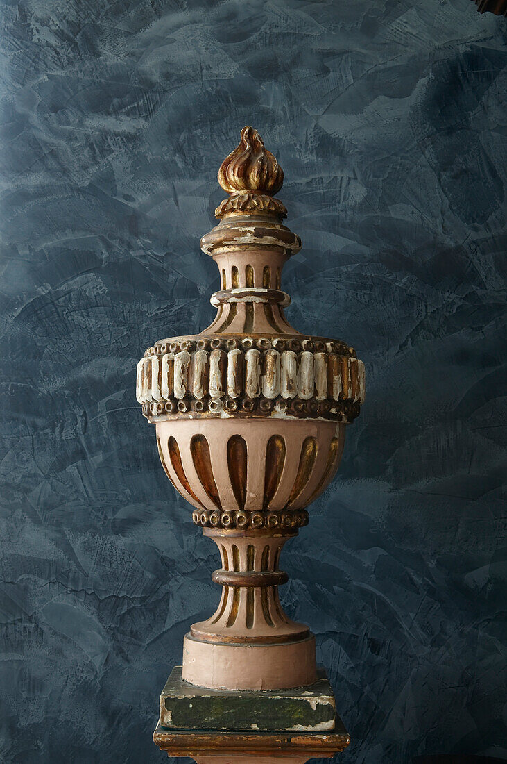 Carved and painted wooden sculpture on pedestal against colour-washed blue wall