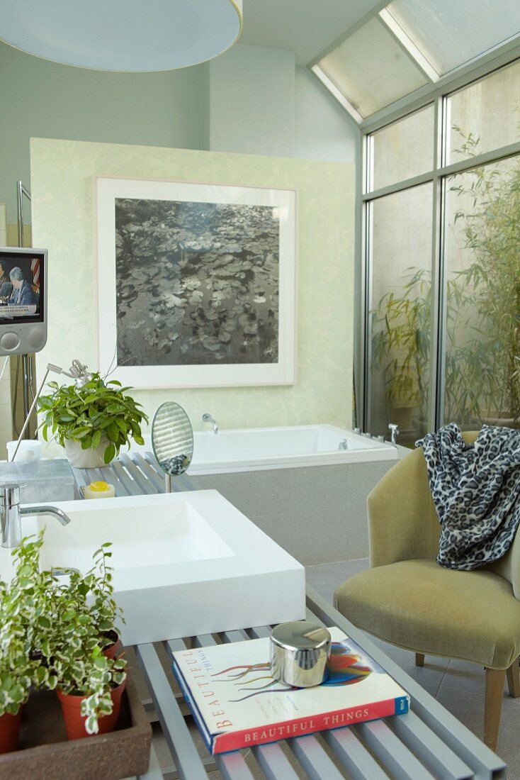Modernes Bad mit Sessel im Retrostil vor Glaswand und Blick auf Gartenpflanzen