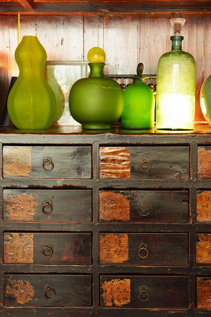 Various green bottles on rustic wooden chest of drawers