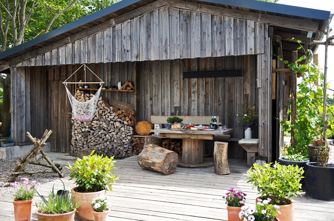 Baumstamm-Hocker, Tisch und gestapeltes Brennholz auf der Terrasse einer Holzhütte