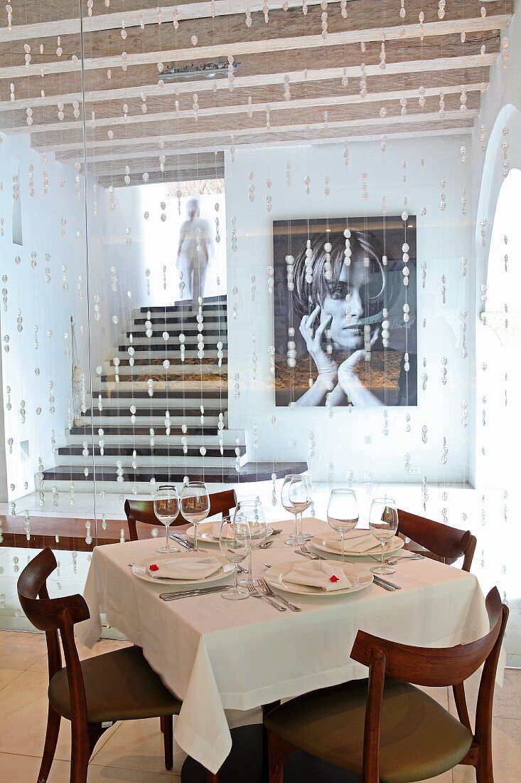 Set table in front of bead curtain in hotel restaurant and view of photo on wall next to recessed staircase