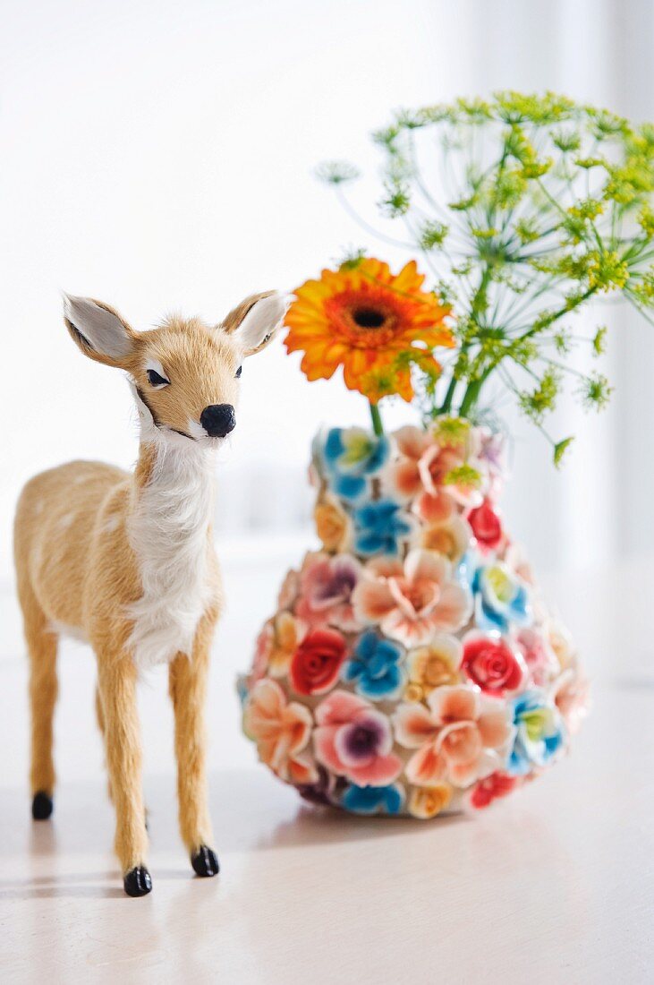 Kleine Rehfigur mit Fell neben blütenbestückter Blumenvase