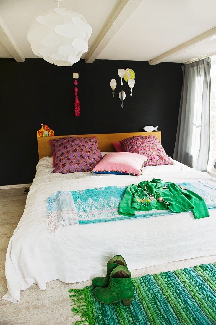 Ungewöhnliche Farbgestaltung im Schlafzimmer mit rosa Dekokissen vor schwarzer Wand und Flickenteppich in Grüntönen