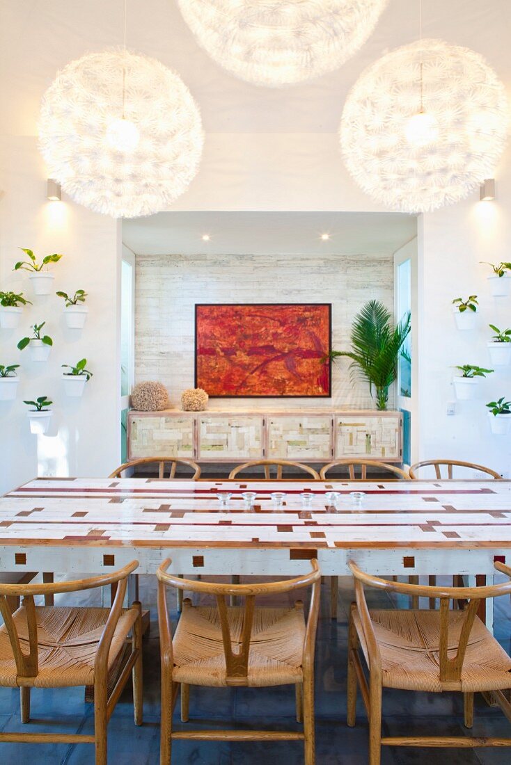 White dining table with wooden inlays and classic, 50s chairs; painting in niche in background