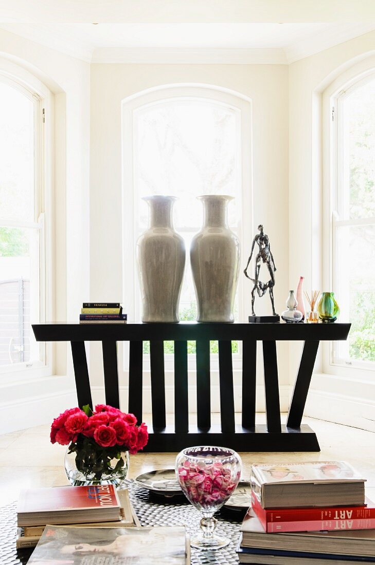 Blick über Tisch mit Blumenstrauss vor Holztheke mit hohen Porzellanvasen im Erker eines Wohnzimmers