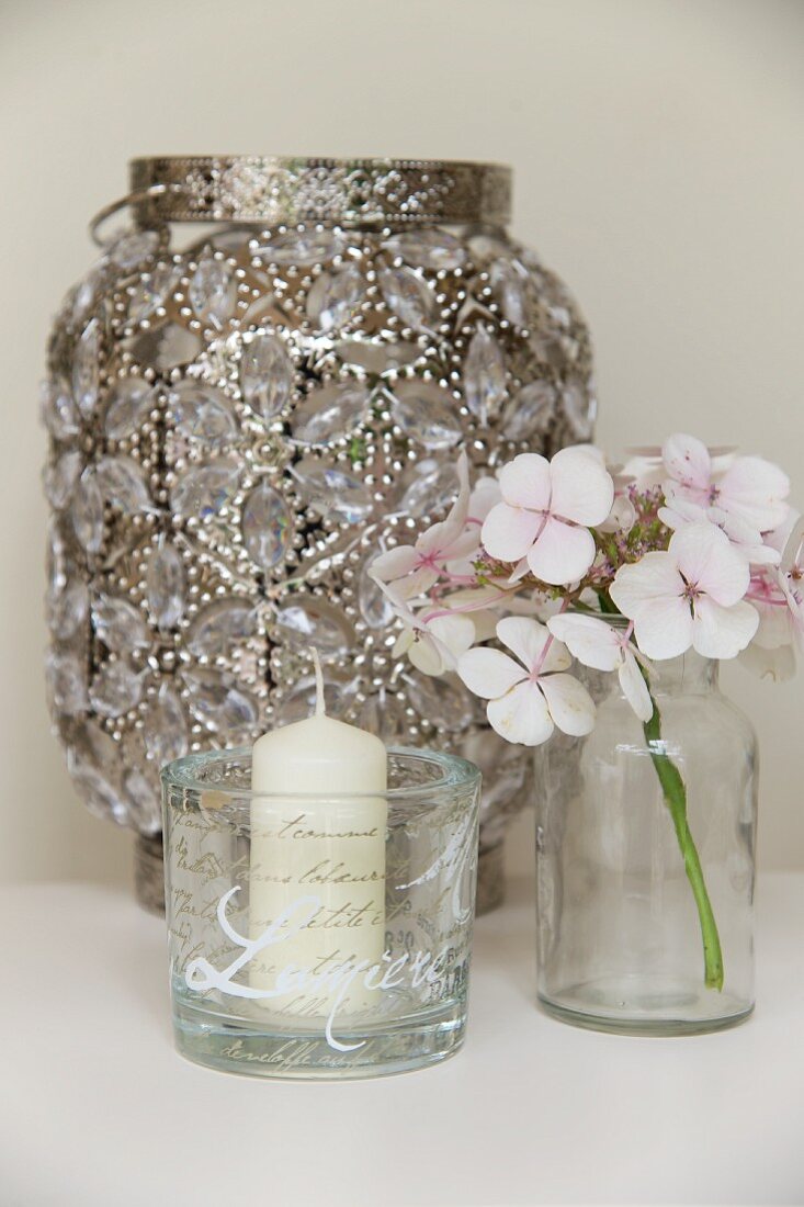 Kerze in einem Glas mit Schriftmuster, Hortensienblüte und antike Laterne mit Schmucksteinen besetz
