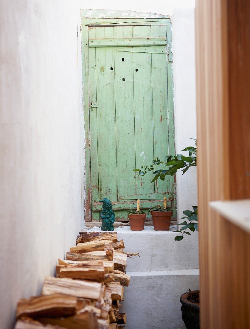 Stacked firewood in entrance area in front of green front door