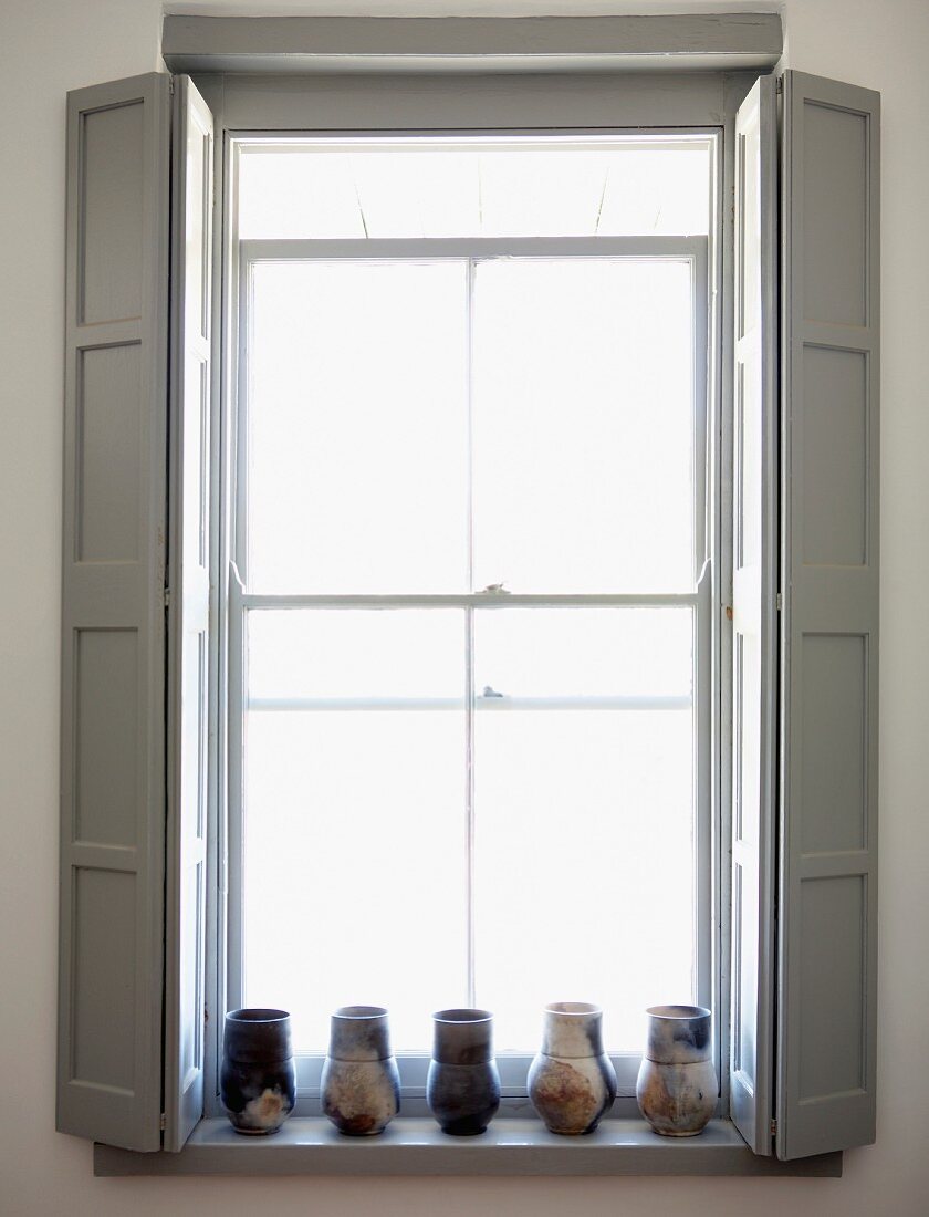 Window with pale grey interior shutters and collection of vases on windowsill