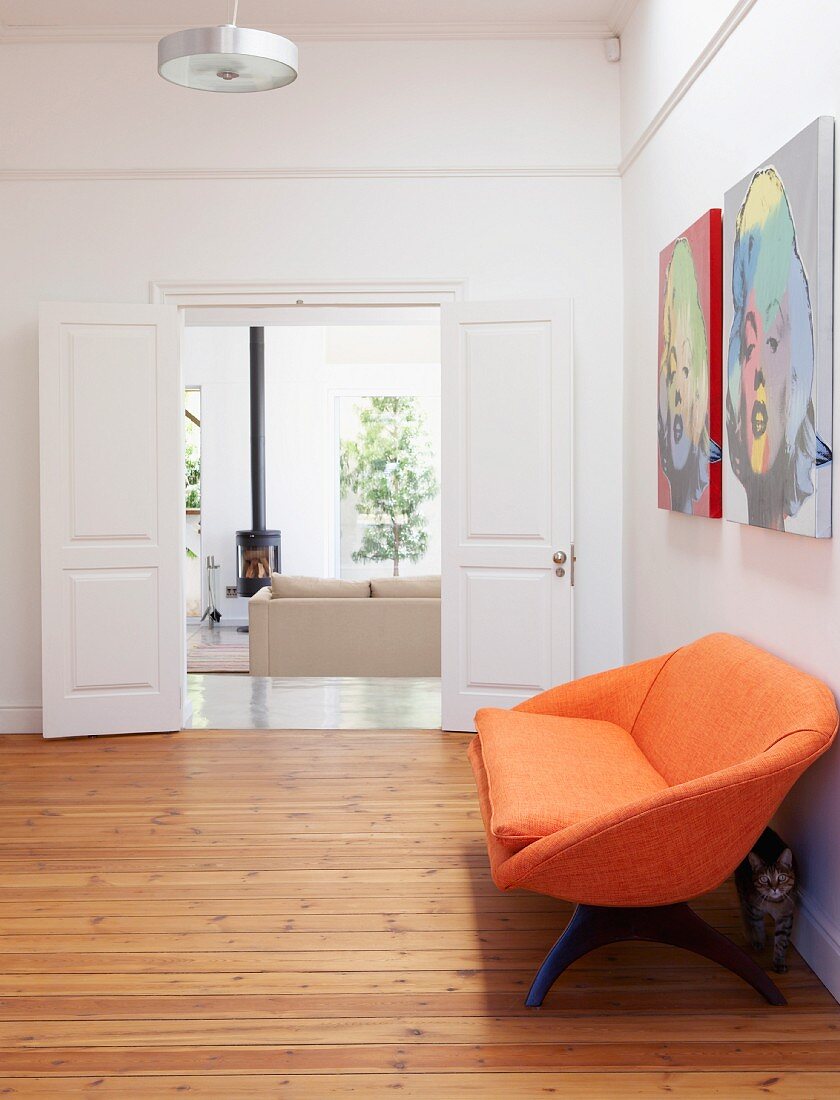 Orangefarbenes Sofa auf Dielenboden im Vorraum mit offener Flügeltür und Blick ins Wohnzimmer