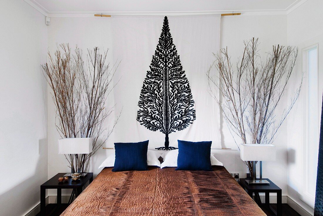 Naturhaft gestaltetes Schlafzimmer mit hohen Zweigbündeln hinter Nachttischen und Wandbehang mit stilisierter Baumdarstellung