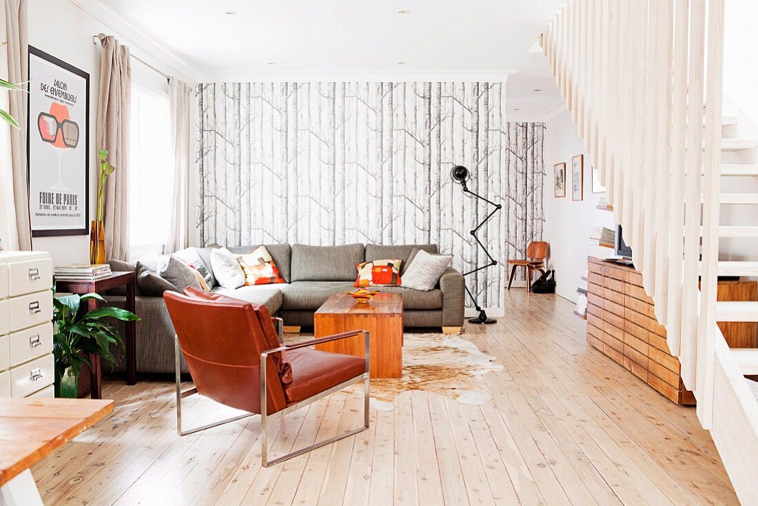 Grosszügiger Wohnraum mit Ledersessel und grauer Couch übereck in offenem Loungebereich gegenüber Treppenaufgang