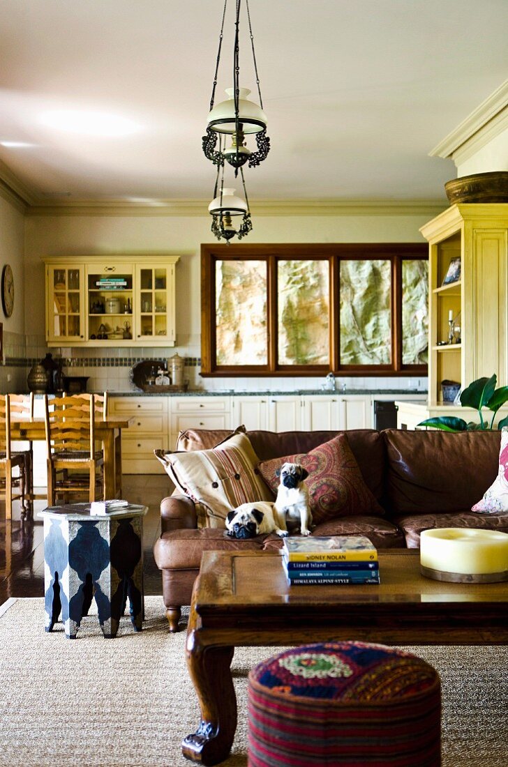 Heavy coffee table and sofa in country-style, open-plan interior with dining area in front of fitted kitchen