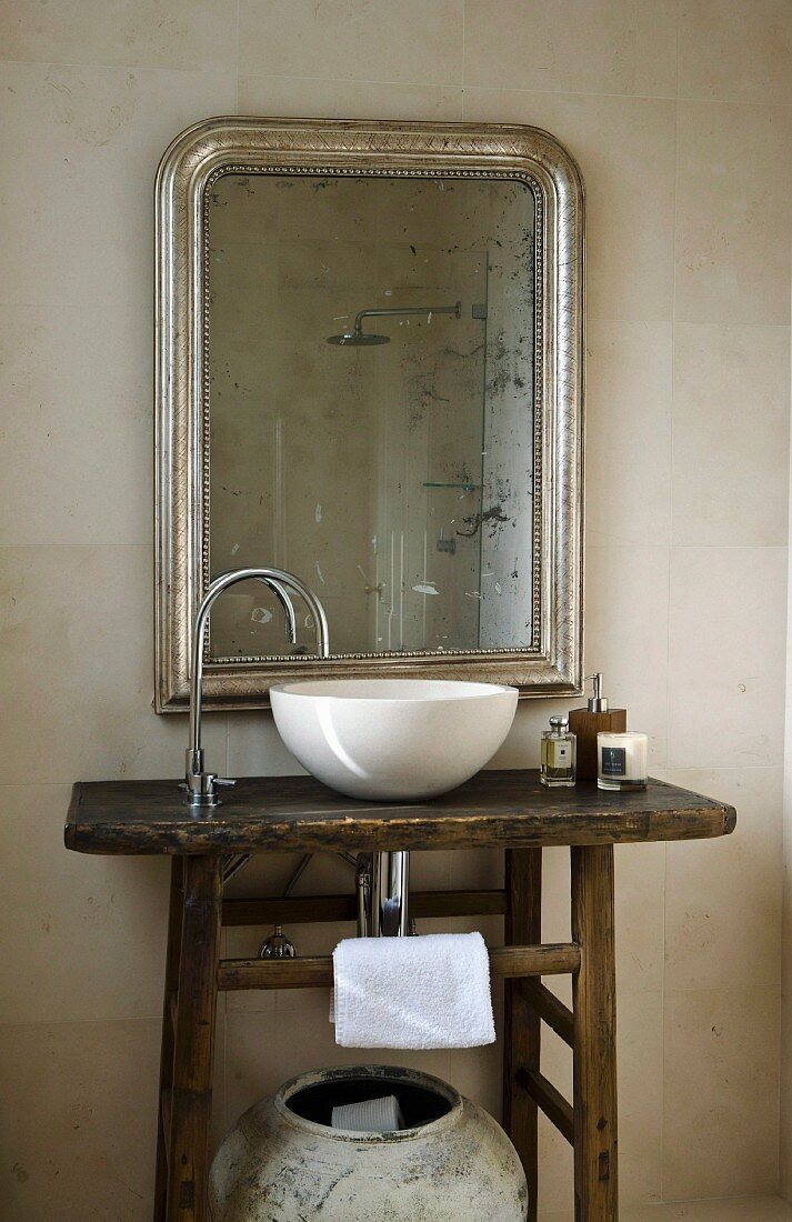 Rustikaler Waschtisch mit weisser Waschschüssel und Designer Armatur vor Spiegel mit Silberrahmen