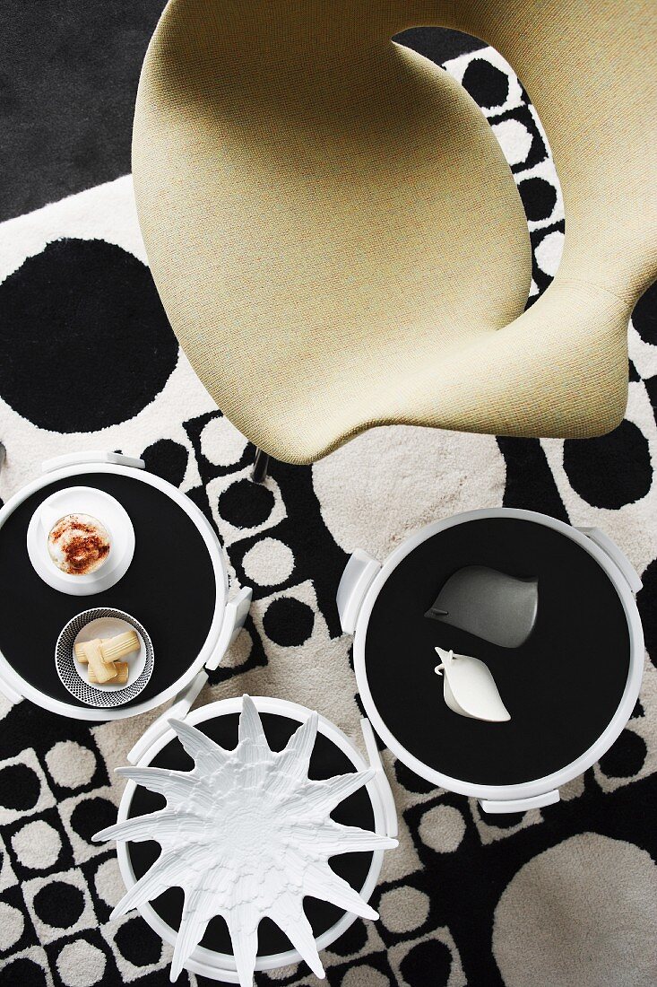 Designerstuhl und dekorierte Beistelltische auf Teppich mit schwarzweissem Kreismuster im 60er Jahre Retrostil