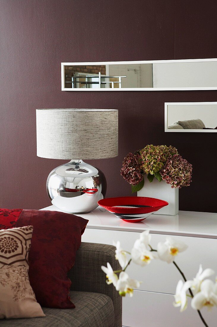 Retro lamp with mirrored, spherical base on sideboard and separate floating shelves on dark-painted wall
