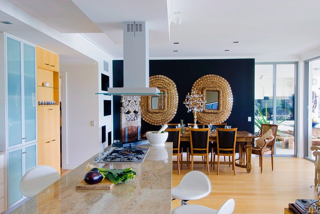 Blick über Küchentheke mit polierter Natursteinplatte auf einen Essplatz mit Goldrahmenspiegeln an schwarzer Wand