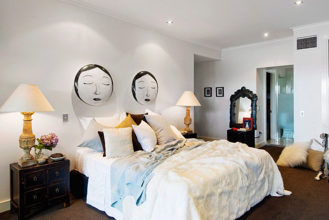 Double bed, bedside lamps and Oriental-style cabinets in bedroom with sculptures of sleeping faces on wall