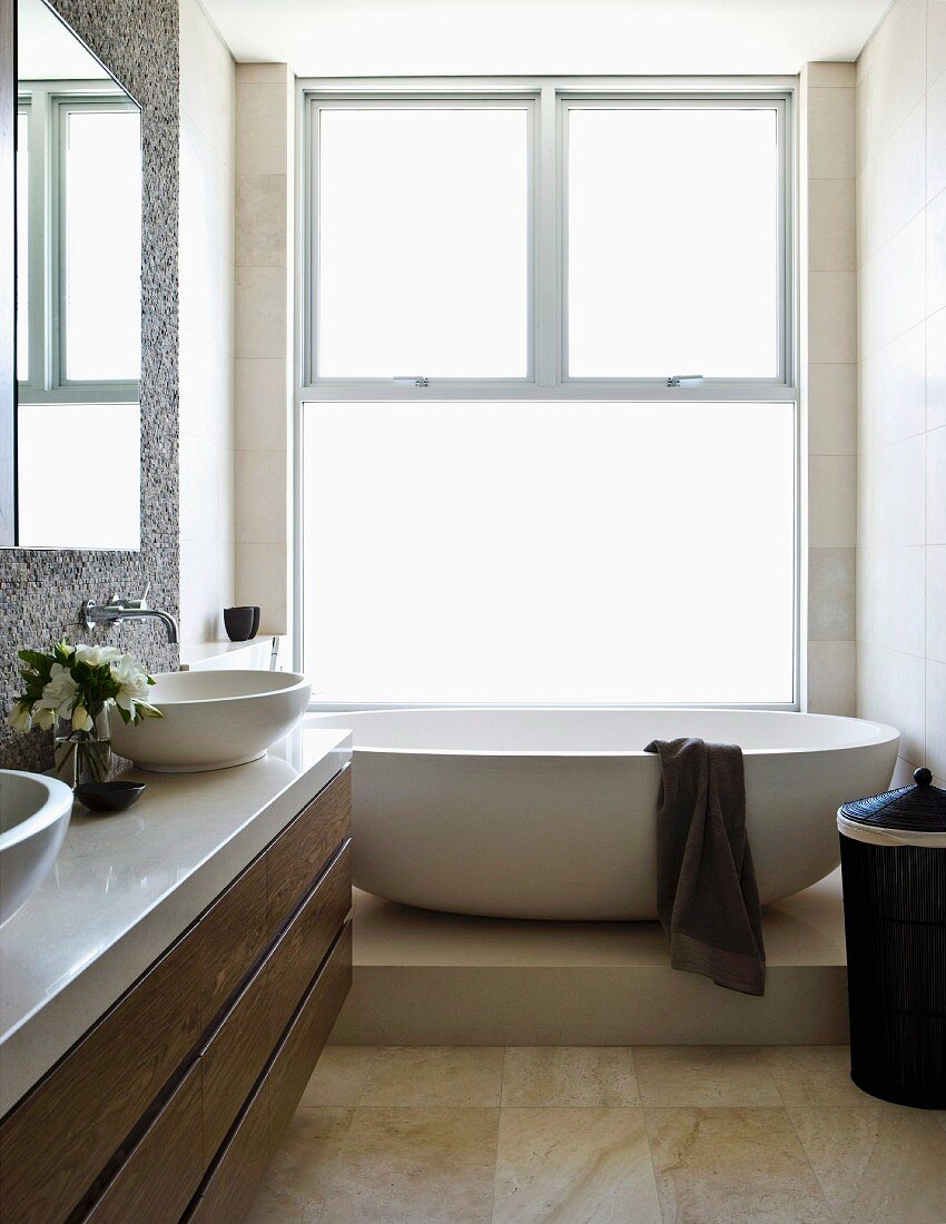 Bathroom with washstand and oval free-standing bathtub on platform in front of floor-to-ceiling sash window