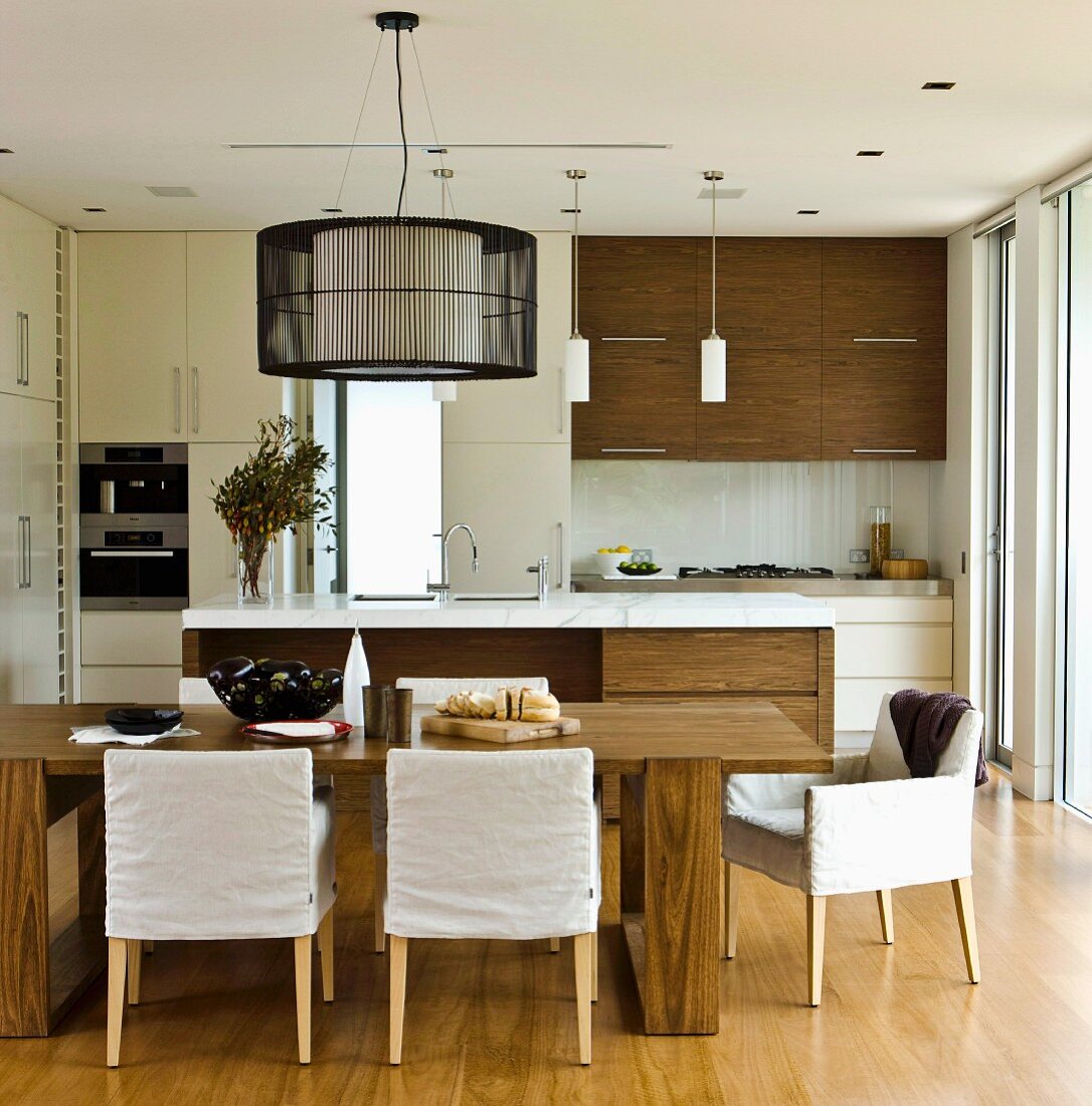 Open-plan kitchen with walnut veneer, dining table and chairs with loose covers