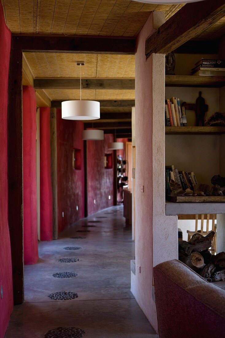 View of a narrow hallway with white hanging lights hanging from the straw ceiling and red, curving wall