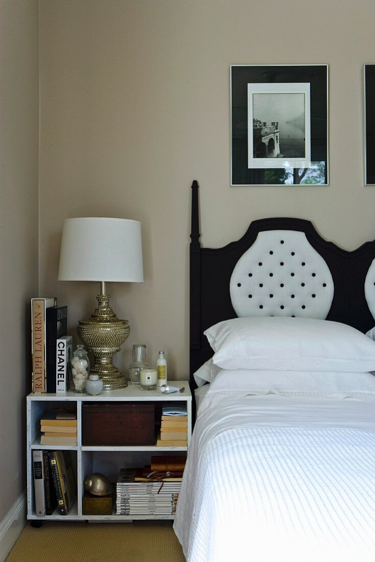 Nightstand with books and elegant table lamp next to a double bed with a black and white headboard