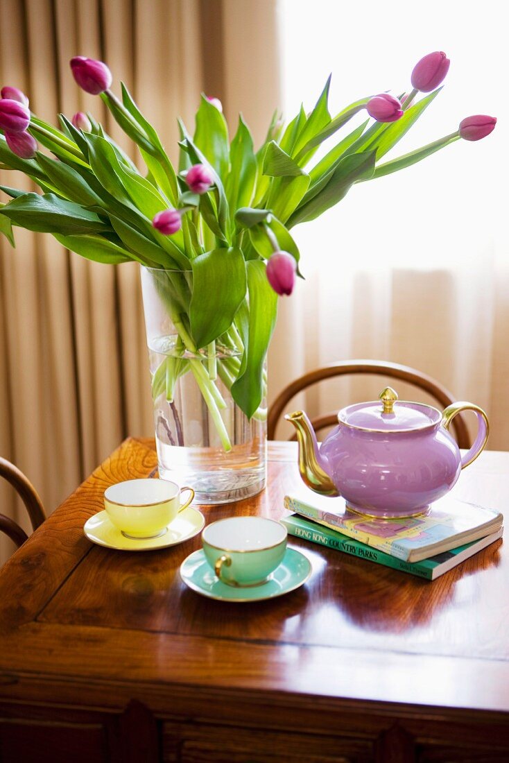 Bouquet of purple tulips in glass vase and gold-rimmed tea set on antique wooden table