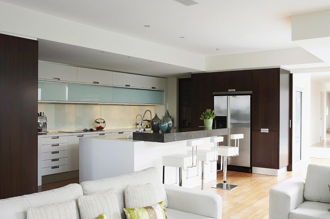 Blick über weiße Sofagarnitur auf Designer Küche mit Mittelblock in Weiß; Einbauschränke mit Holzfronten