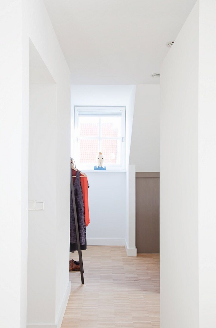 View along open corridor with view of clothes rack and window in attic interior